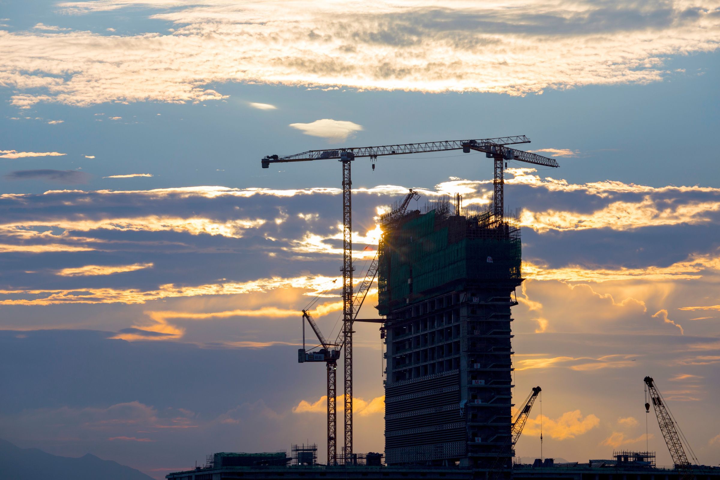 A tower under construction with cranes against an evening sky